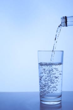 fresh clean water is poured from a bottle into a glass cup. Light background.. Hight quality photo