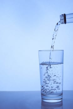 fresh clean water is poured from a bottle into a glass cup. Light background.. Hight quality photo