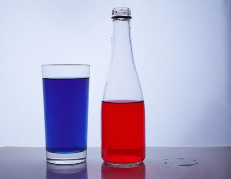 bottle and glass. In which the red and blue liquids are poured on a white background. Hight quality photo