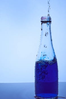 a blue liquid is poured into a glass bottle. Light blue background. Hight quality photo