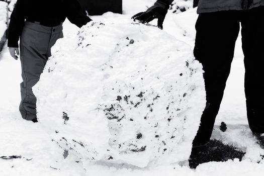 Black and white image of a child rolling a large snowball in the winter season snow to make a snowman stock photo
