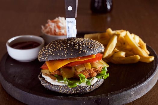 Black burger with sesame seeds with fries and salad of cabbage closeup photo