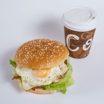 burger with egg and salad on a white background. Nearby is a paper cup with a coffee closeup photo