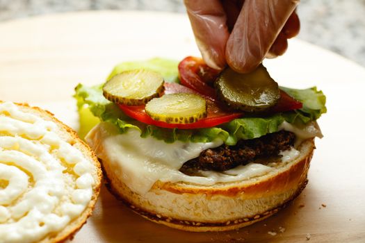 Man's hand puts pickled cucumber on a bun for a burger closeup photo