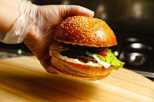 Man's hand in gloves holds juicy burger against dark closeup background Beautiful concept background