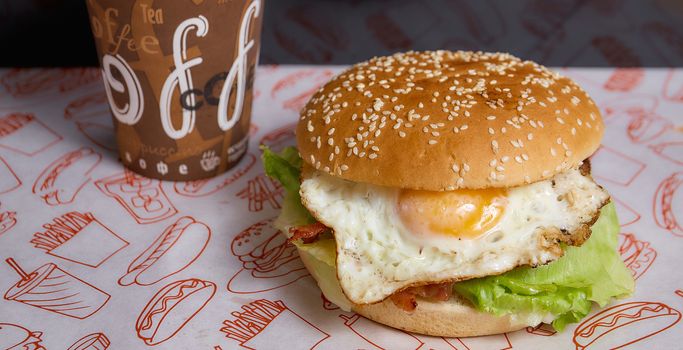 burger with egg and salad on a white background. Nearby is a paper cup with a coffee closeup photo