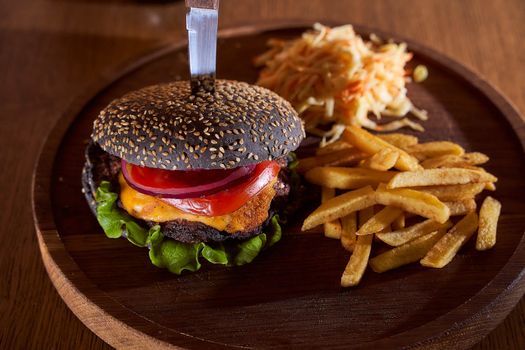 Black burger with sesame seeds with fries and salad of cabbage closeup photo