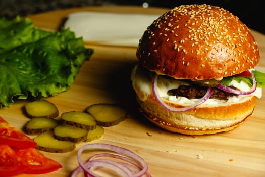 Juicy burger, sliced cucumbers, salaa leaves and tomatoes lie on a wooden tray Beautiful concept background