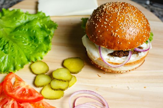 Juicy burger, sliced cucumbers, salaa leaves and tomatoes lie on a wooden tray Beautiful concept background