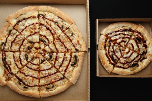 Large and small pizzas lie on an open cardboard box. Black background top view photo
