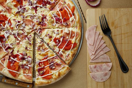 Pizza sliced into pieces lies on a wooden background. Nearby fork and sliced ham Beautiful concept background