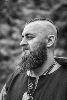 Viking portrait with thick beard, black and white image of historical re-enactment among medieval ruins