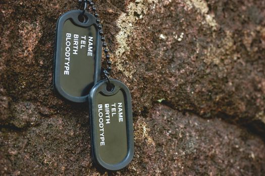 Military tag hanged on the rock on the rock background in forest. Concept of soldier sacrifice and armistice. Closeup and copy space.