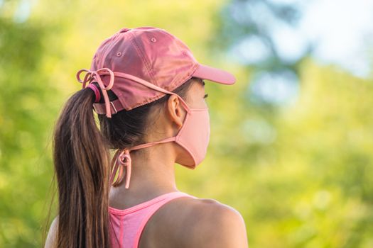 Corona virus face mask COVID-19 young healthy woman on outdoor walk wearing cloth string ties with pink sports cap. Summer lifestyle.