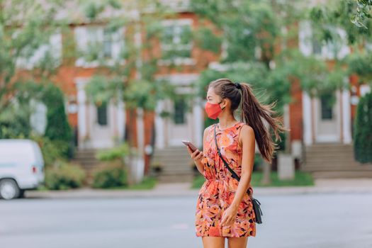 COVID-19 girl walking in city street wearing face mask. Mandatory wear Asian woman commuting using mobile phone. protection as prevention for coronavirus outside in city park summer lifestyle outdoor. Corona virus.