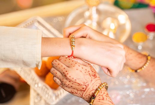 Closeup of hands, sister tying rakhi, Raksha bandhan to brother's wrist during festival or ceremony - Rakshabandhan celebrated across India as selfless love or relationship between brother and sister.