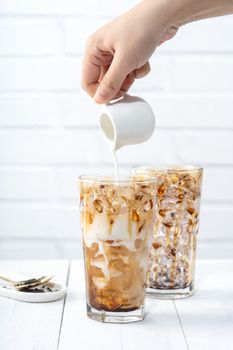 Making bubble tea, pouring blend milk tea into brown sugar pattern drinking glass cup on white wooden table background, close up, copy space