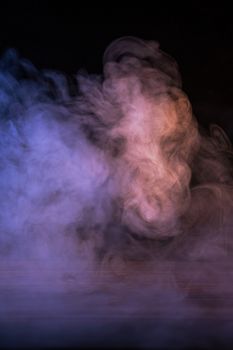 Conceptual image of multi-colored smoke isolated on dark black background and wooden table.