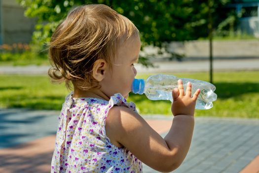 Little girl drinks water from a bottle. Side view. Close-up.