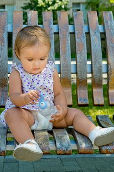 Little girl sits on a park bench with a bottle of water in her hands.