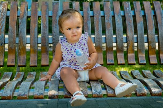 Little girl sits on a park bench with a bottle of water in her hands.