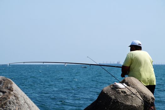 Varna, Bulgaria - July, 19, 2020: fat man fishing with a rod at the sea