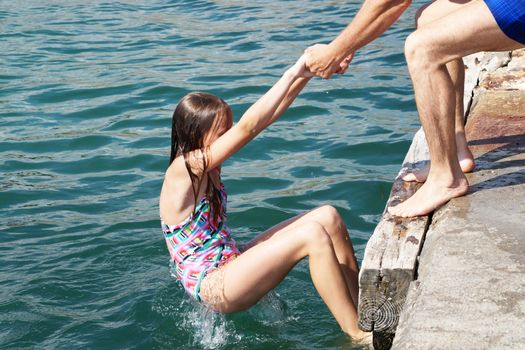 a man helps a girl to climb the pier from the sea