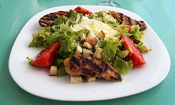 Caesar salad with chicken and cheese on a large white plate