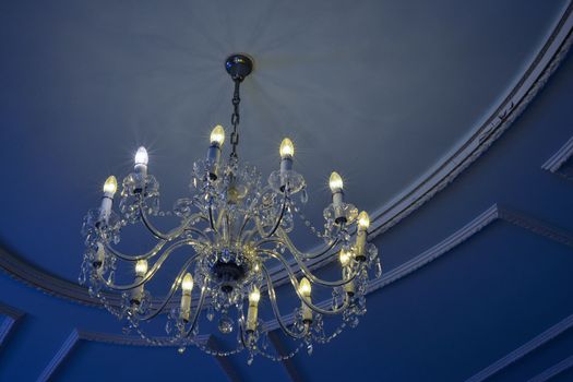 Comparison of energy saving vs regular bulbs in a glass chandelier under a blue ceiling.