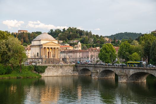 Turin, Piedmont, Italy. July 2020. Wonderful evening view of the Gran Madre church overlooking the Po river. The waterfall downstream of the dam is highlighted. On the bridge people and cars.