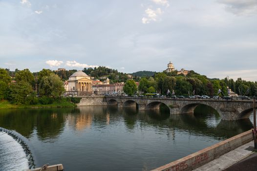 Turin, Piedmont, Italy. July 2020. Wonderful evening view of the Gran Madre church overlooking the Po river. The waterfall downstream of the dam is highlighted. On the bridge people and cars.