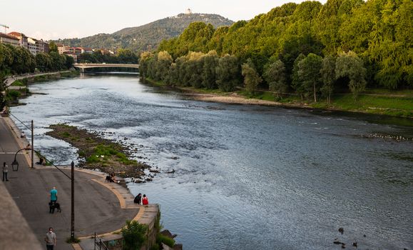 Turin, Piedmont, Italy. July 2020. Beautiful evening view of the Po river. People enjoy relaxing along the river and the panorama of the Turin hill.