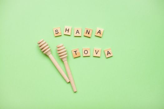 Words from wooden blocks "shana tova" and wooden spoons for honey on a green background. Rosh hashanah