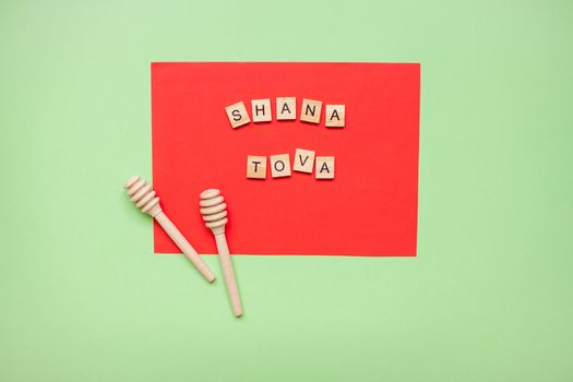 Words from wooden blocks "shana tova" and wooden spoons for honey on a red and green background. Rosh hashanah