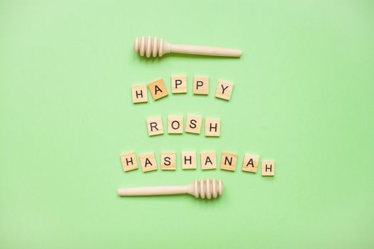 Words from wooden blocks 'happy rosh hashanah' and wooden spoons for honey on a green background