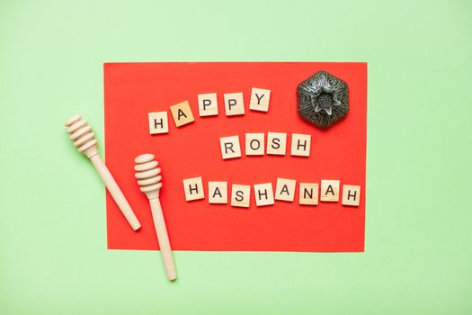 Words from wooden blocks 'happy rosh hashanah' and wooden spoons for honey on a red and green background