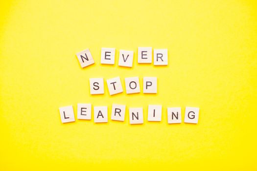 Words from wooden blocks "never stop learning" on bright yellow background