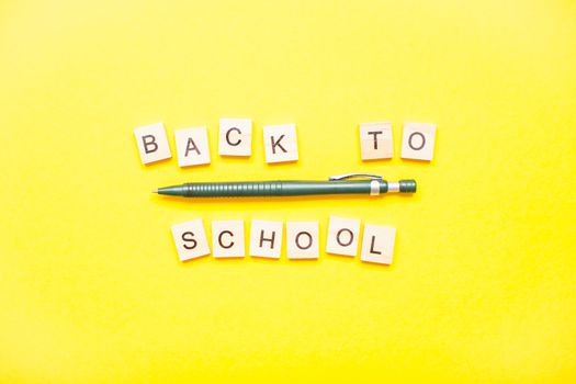 Words from wooden blocks "back to school" and stationery on bright yellow background