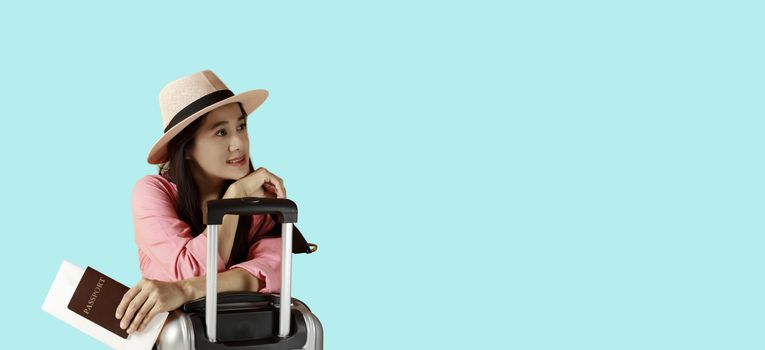 Asian women long hair wear Straw hat in hand holding passport book and sunglasses  with travel bag copy space banner. Femail to travel with suitcase and passport on blue background. Summer concept.