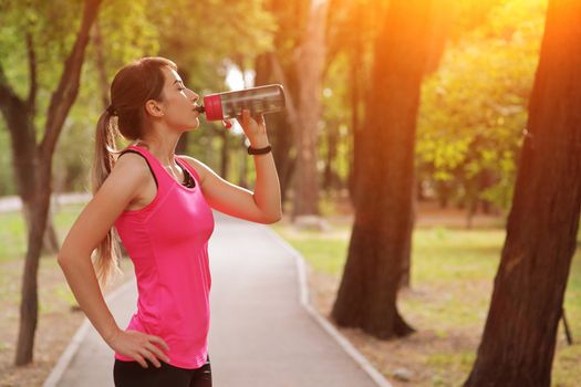 Beautiful fitness athlete runner woman drinking water in the park. Portrait face of a young woman holding a water bottle in summer. Forest