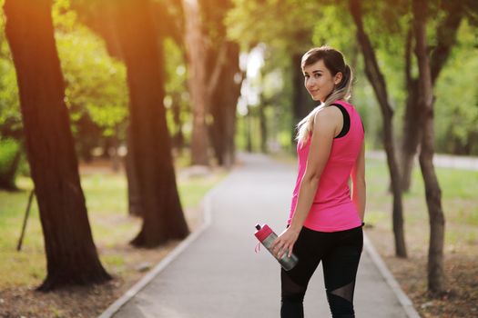 Beautiful fitness athlete runner woman drinking water in the park. Portrait face of a young woman holding a water bottle in summer. Forest