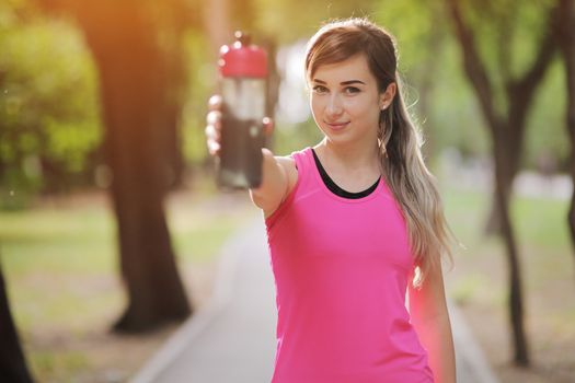 Beautiful fitness athlete runner woman drinking water in the park. Portrait face of a young woman holding a water bottle in summer. Forest