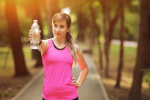 Beautiful fitness athlete runner woman drinking water in the park. Portrait face of a young woman holding a water bottle in summer. Forest