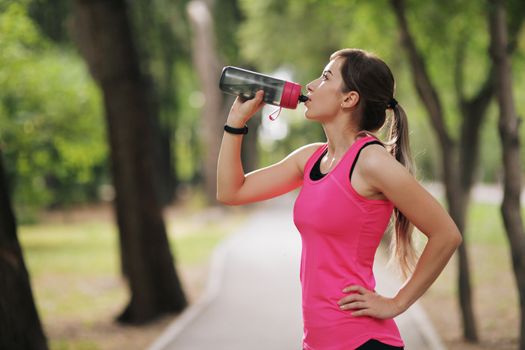 Beautiful fitness athlete runner woman drinking water in the park. Portrait face of a young woman holding a water bottle in summer. Forest