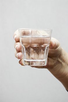 Hand with glass of water on gray background