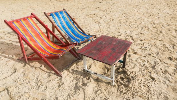 Red and blue beach chair with red wood table on the beach. Summer concept in warm sun light