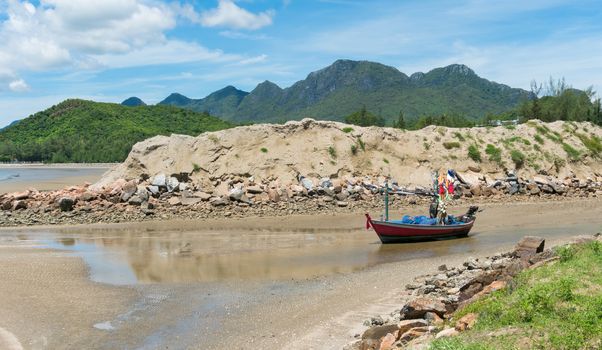 Red fishing boat on beach and green hill and sea and reef or rock. Fisherman boat or fishing boat for summer concept at Prachuap Khiri Khan 
Thailand