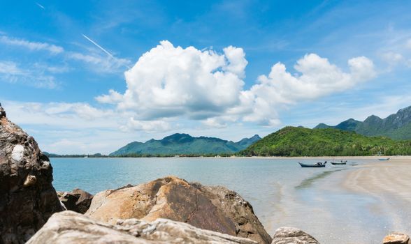The beach or sea with blue sky and fishing boat and green mountain and stone in Prachuap Khiri Khan, Thailand. Attractions in Prachuap Khiri 
Khan Thailand. Summer concept or relaxation