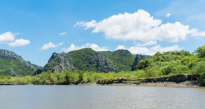 Stone or rock mountain or hill with green tree and blue sky and water and cloud at Khao Dang canal Prachuap Khiri Khan Thailand. Landscape or 
scenery summer concept for boat trip