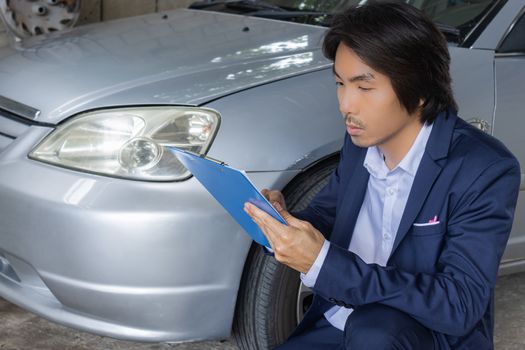 Asian Insurance Agent or Insurance Agency in Suit Reading Report and Inspecting Car Crash from Accident for Claim at Outdoor Place